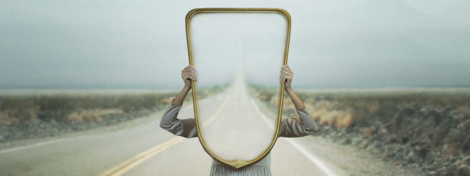 the woman hides holding a mirror in front of her face; introspection path concept