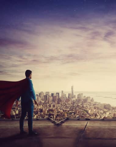 Rear view confident businessman, red cape suit, as hero stands o
