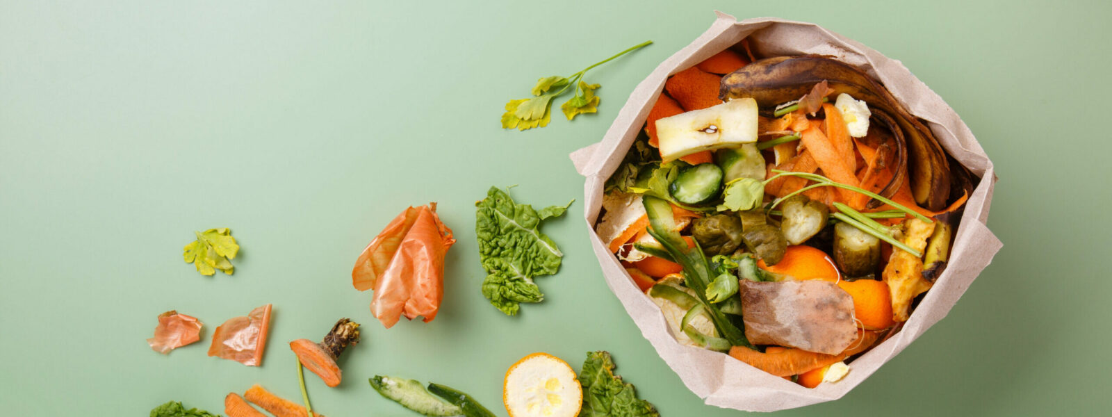 Sorted kitchen waste in paper eco bag on green background. Compo