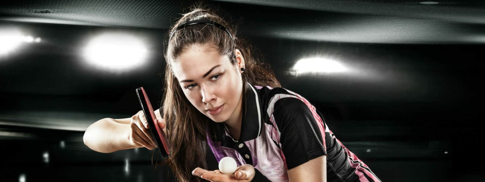 Young pretty sporty girl playing table tennis on black