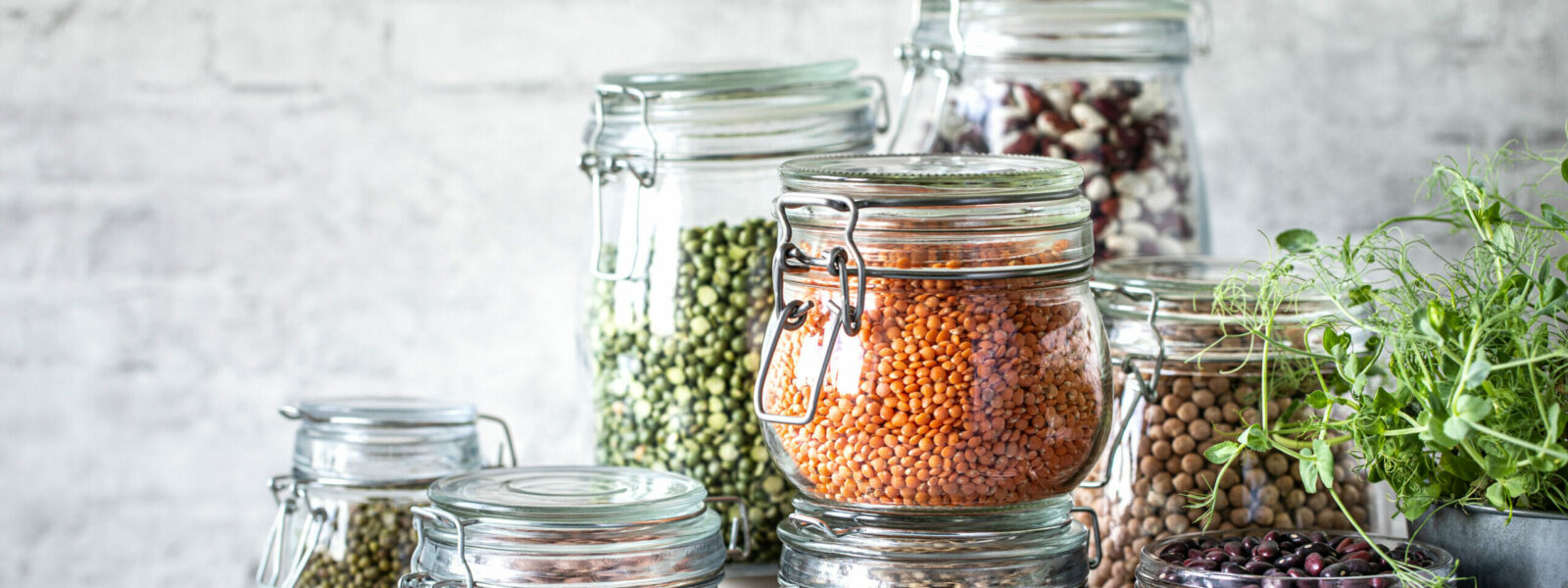 Set of different legumes in glass jars on, concrete white table. A source of protein for vegetarians. The concept of healthy eating and food storage.