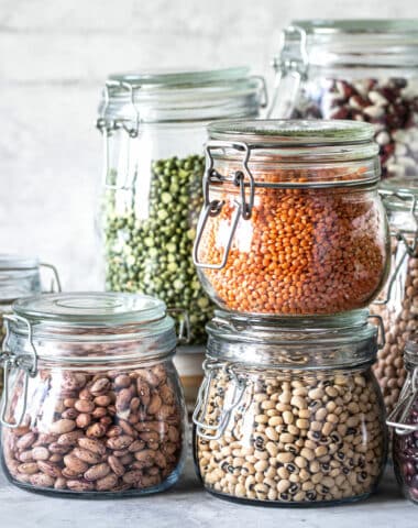 Set of different legumes in glass jars on, concrete white table. A source of protein for vegetarians. The concept of healthy eating and food storage.