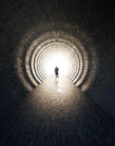 Concept or conceptual dark tunnel with a bright light at the end or exit as metaphor to success, faith, future or hope, a black silhouette of walking man to new opportunity or freedom 3d illustration