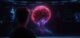 A person observes a glowing brain display on a screen